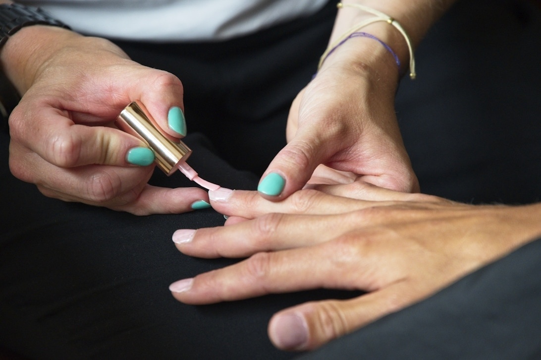 En instruktör visar en student hur man applicerar rosa nagellack på ett korrekt sätt.